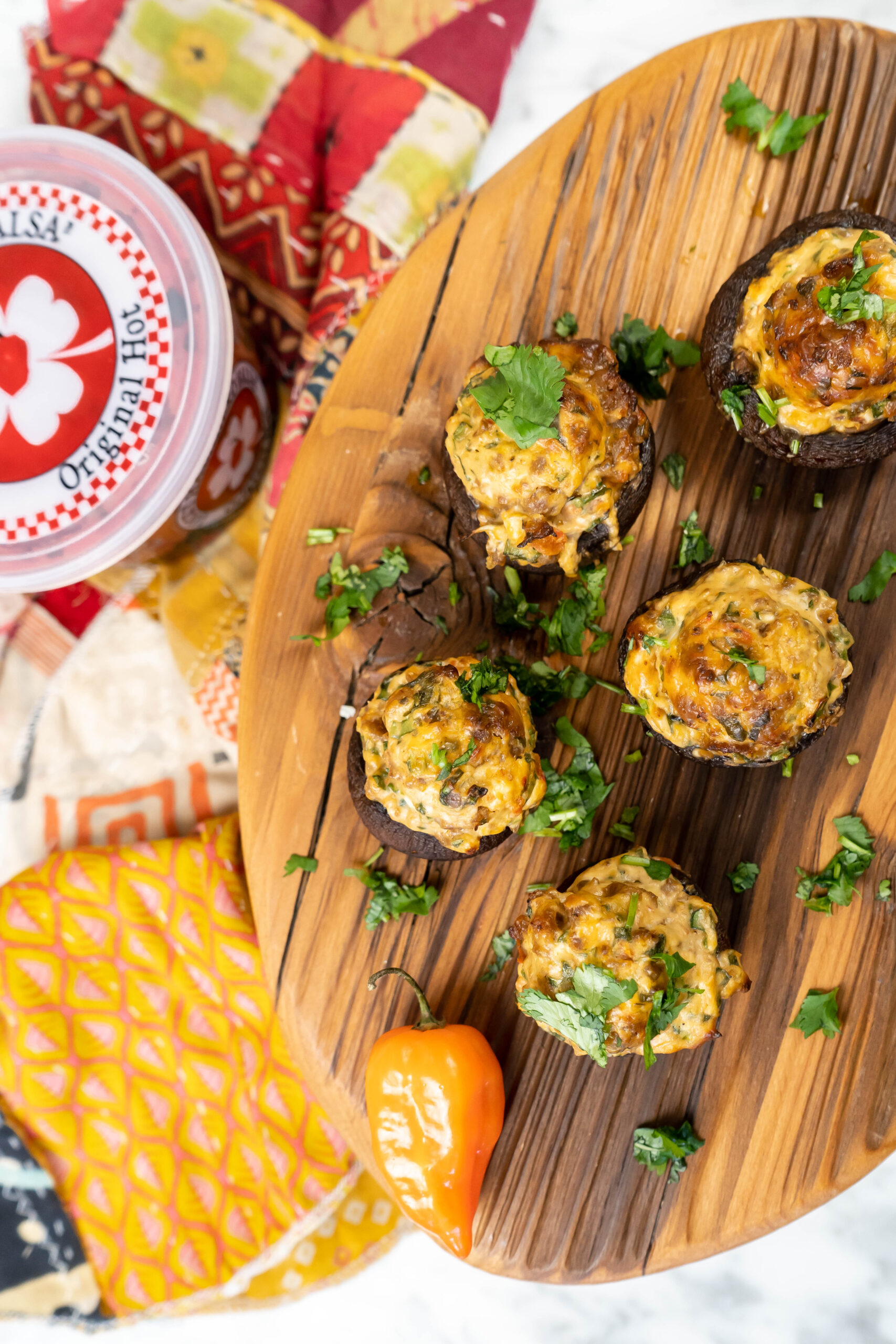 A wood board with stuffed mushrooms and a container of salsa to the left side.