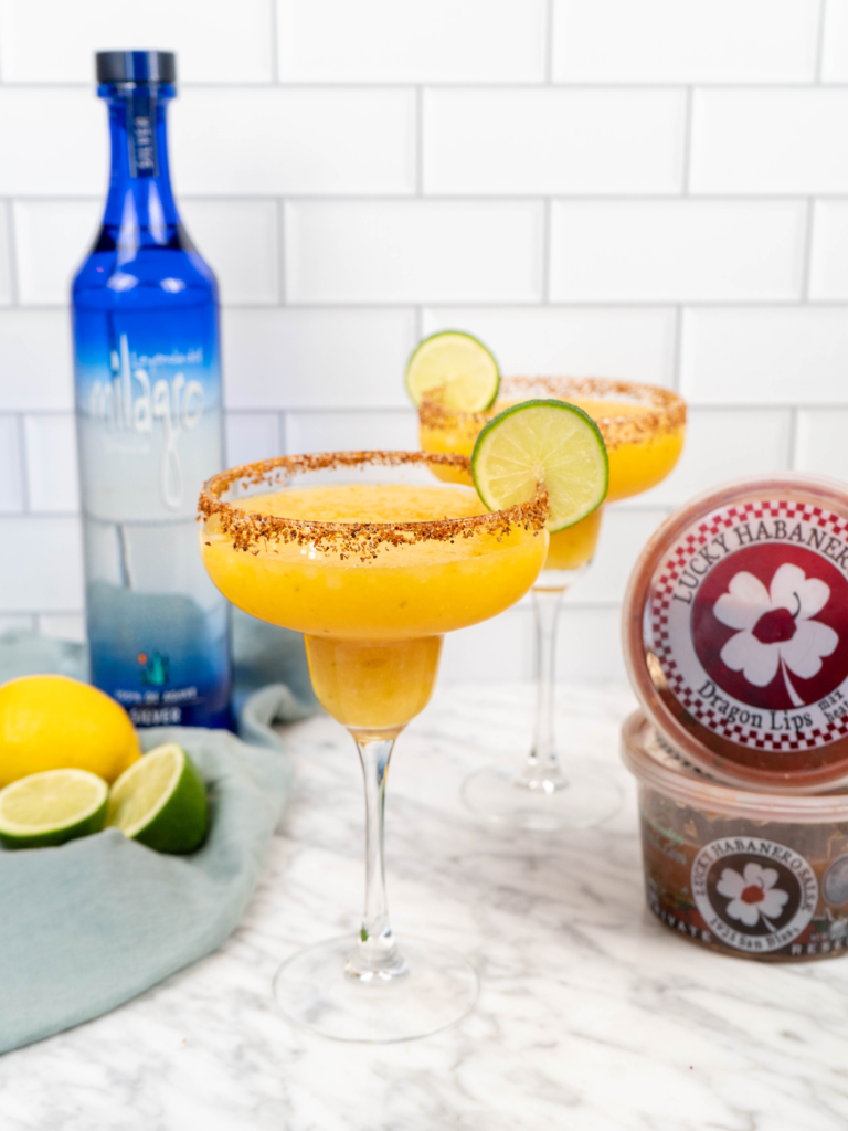 A Margarita with a bottle of vodka and Lucky Habanero salsa in the background of a kitchen counter.