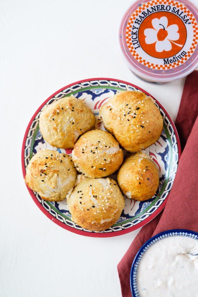 Cream Cheese & Lucky Habanero Salsa-stuffed bagel bites on a decorative plate, next to a container of Lucky Habanero salsa.
